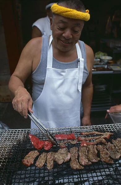 20060651. JAPAN Honshu Tokyo Tsukiji Fish Market. Man cooking red meat on an open grill