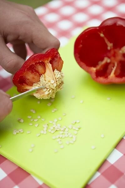 Woman using small kitchen knife to remove seeds from sliced red bell pepper on chopping board on picnic table, close-up