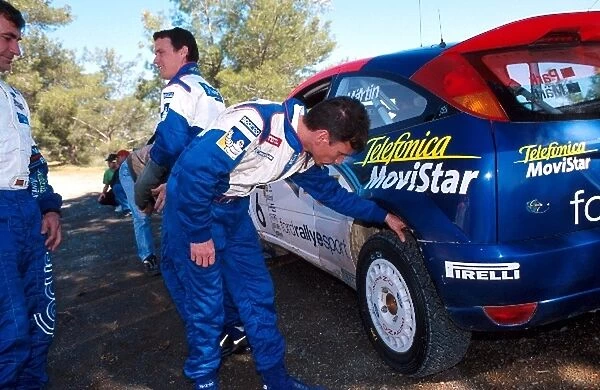 World Rally Championship: Gilles Panizzi Peugeot examines the tyres of Markko Martins Ford Focus