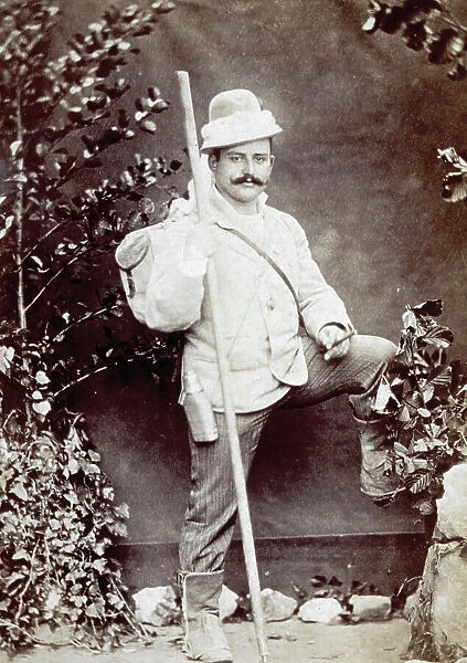 Full-length portrait of a young man dressed for an outing, with a stick in his hand. He is shown against a backdrop with bushes
