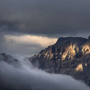 Sunset on Croda Rossa d Ampezzo mountains surrounded by the fog and darkness with only a few spots of sun light, Dolomites, Veneto, Italy, Europe