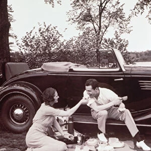 Couple picnicking, man sitting on car runningboard (B&W sepia tone)