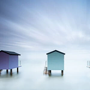 A long exposure shot of 3 beach huts at high tide