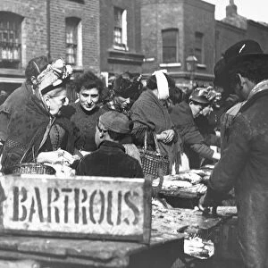 Magic lantern slide circa 1880, Victorian / Edwardian Social History. A fishmonger stall in the market with lots of people buying fish, including children and a lady with a bandage on her chin, perhaps from dental work
